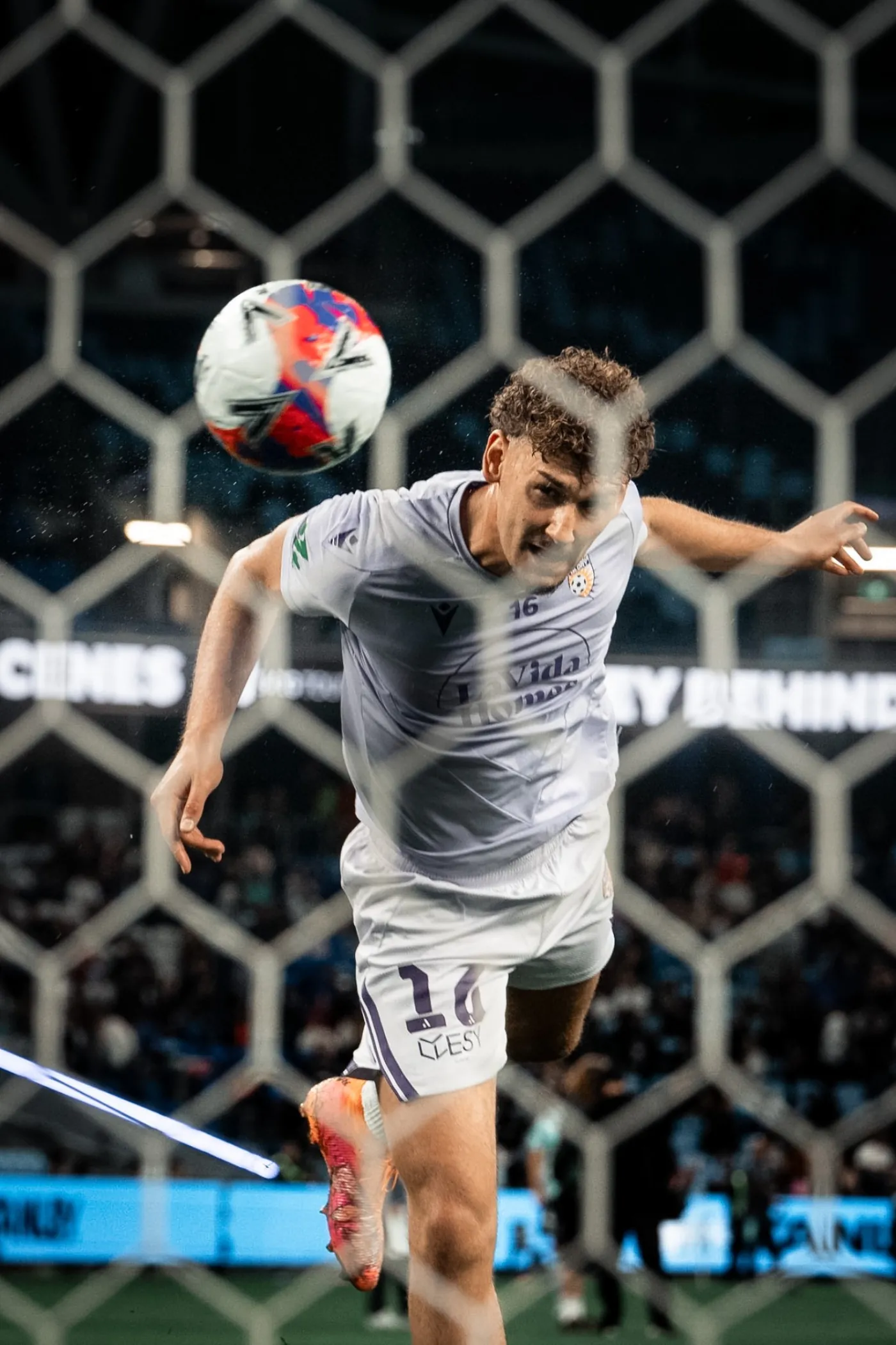 Perth Glory player heading the ball seen through the goal net